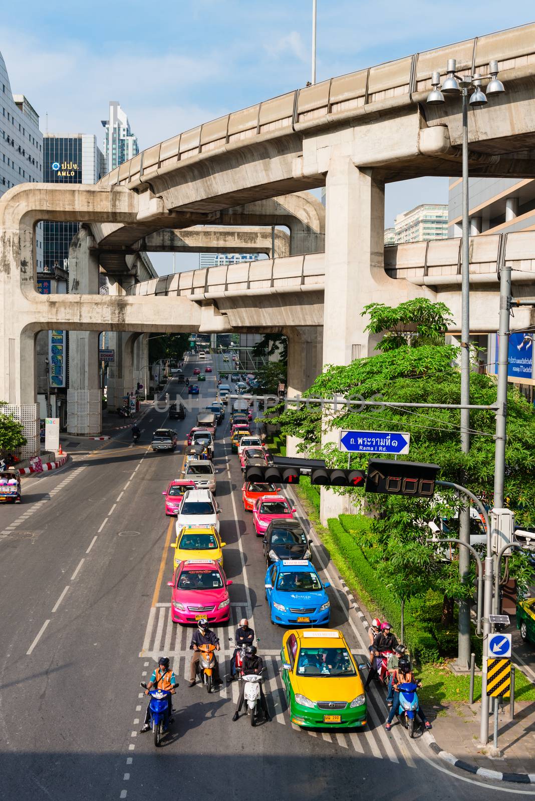 BANGKOK, THAILAND - 21 NOV 2013: Motorbikes and cars stop on traffic light with two level skytrain tracks above street