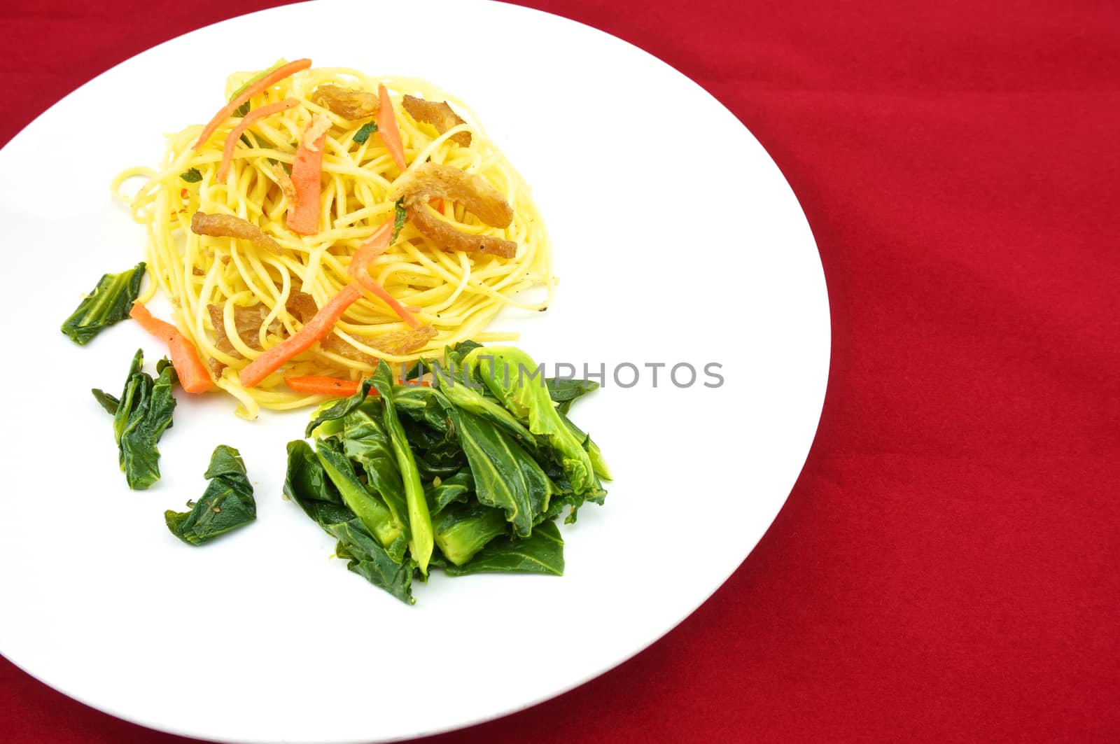 Long life noodle fried with kale, carrots and vegan protein dry on a plate with red background.