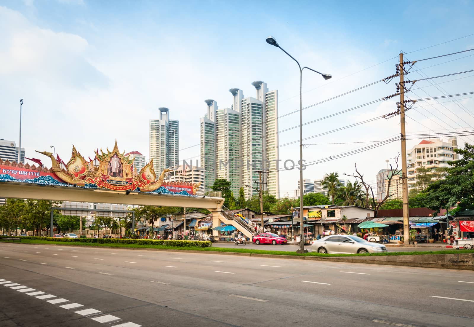 BANGKOK, THAILAND - 21 NOV 2013: Wide street under bridge with portrait of the King of Thailand Bhumibol Adulyadej (Rama IX) and modernt buildings skyscrapers on background