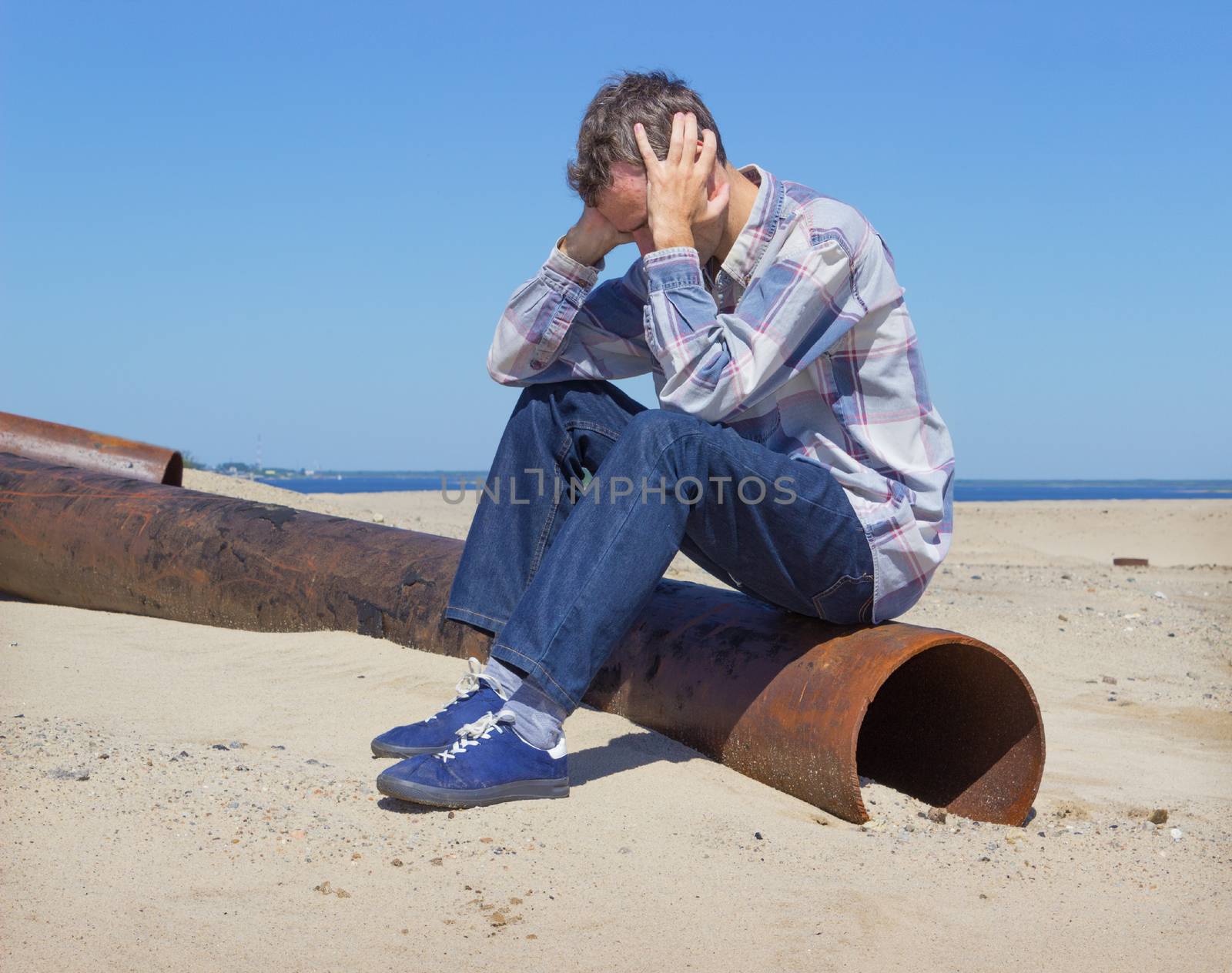 Lonely young man, suffering from depression sitting on wasteland