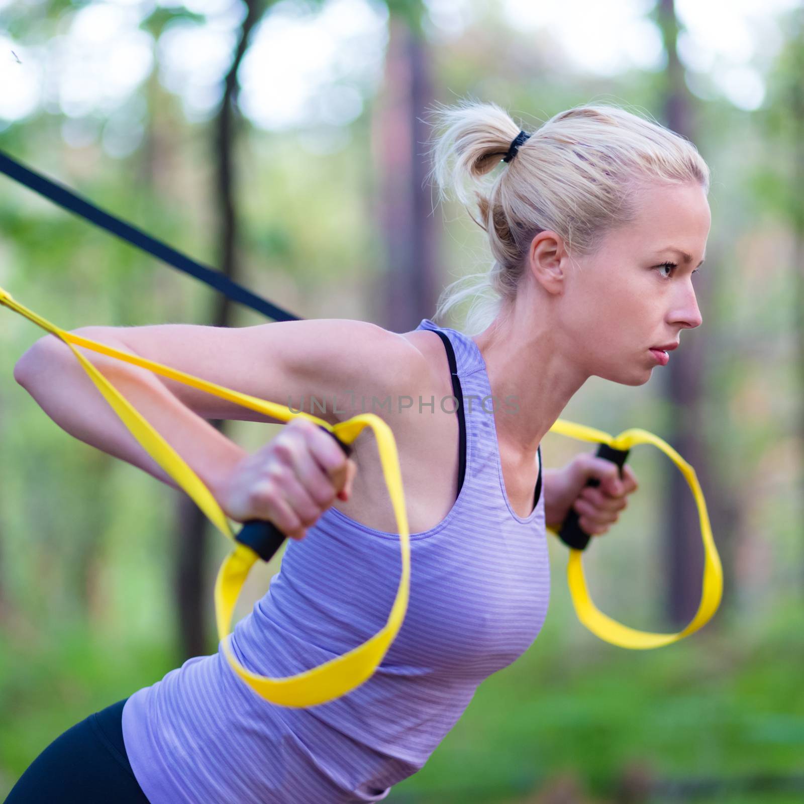 Young attractive woman does suspension training with fitness straps outdoors in the nature.