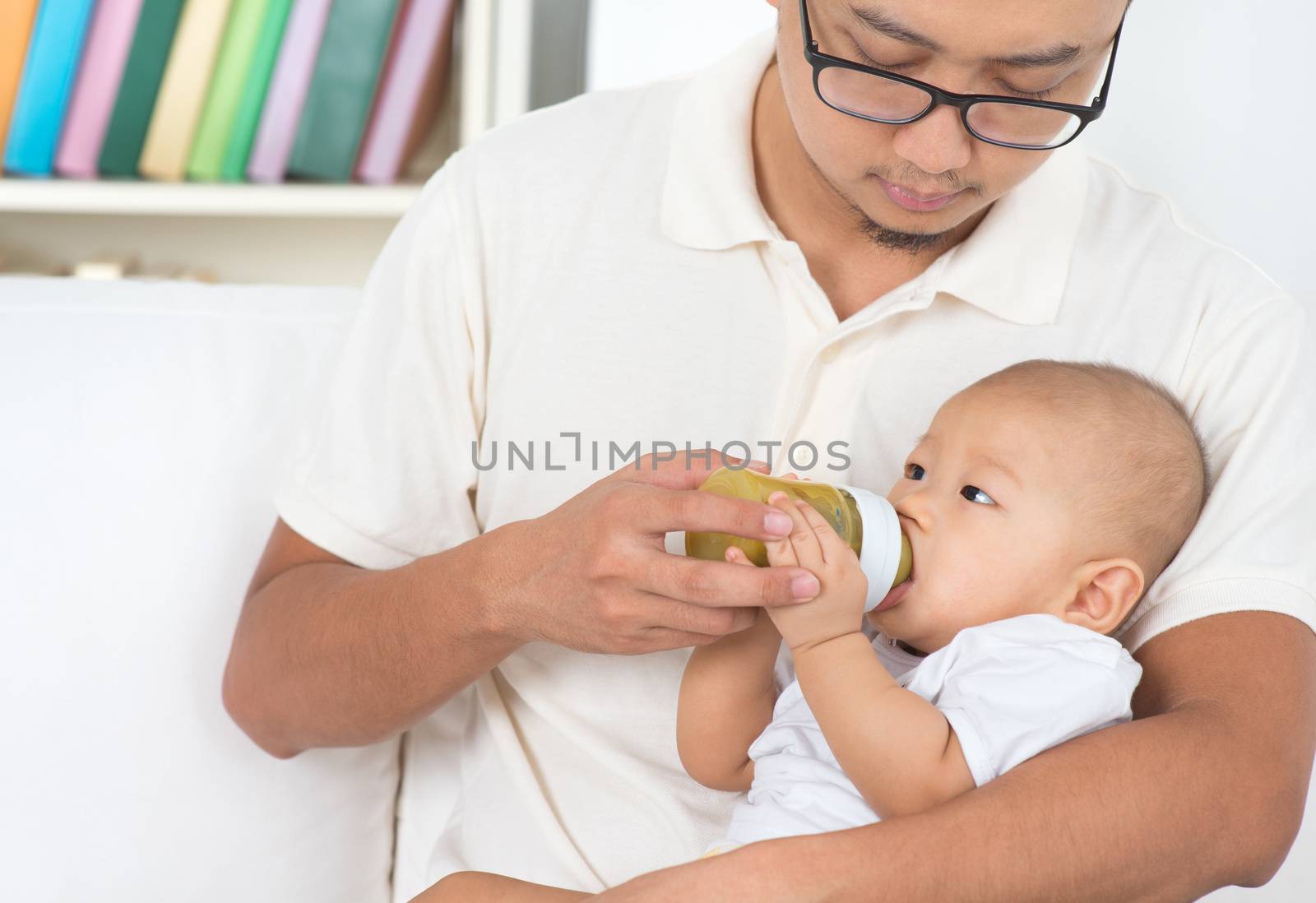 Father bottle feeding baby at home. by szefei