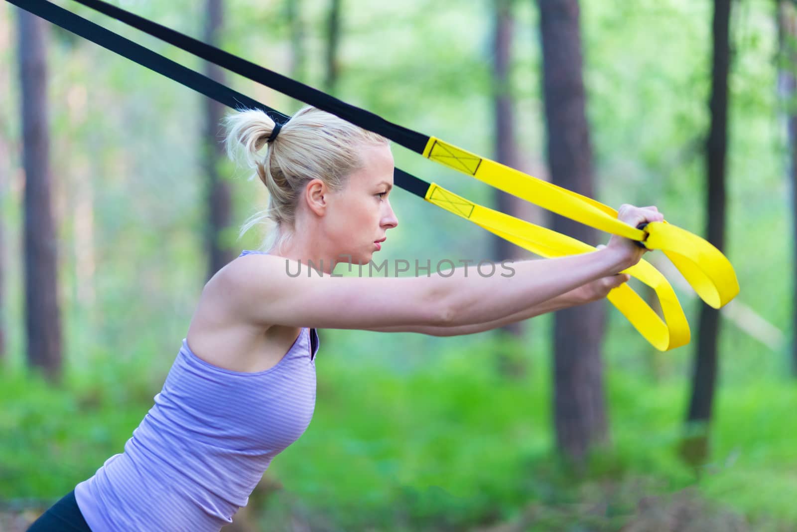 Young attractive woman does suspension training with fitness straps outdoors in the nature.