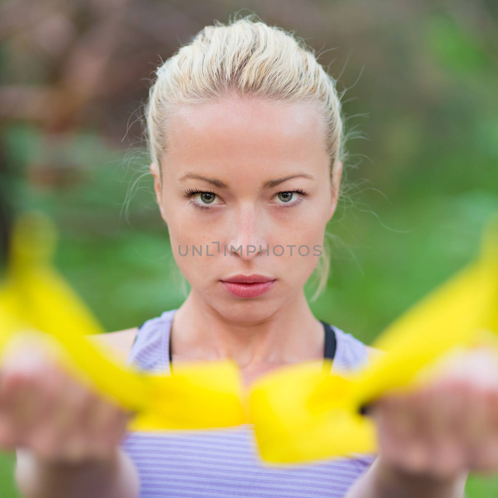 Young attractive woman does suspension training with fitness straps outdoors in the nature.