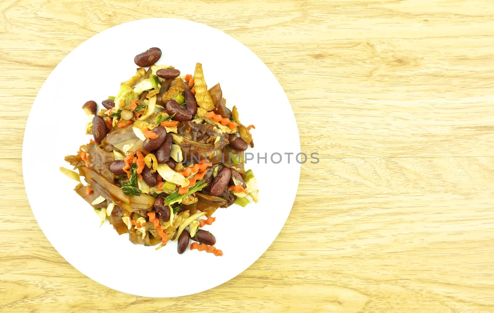 Fired thin noodles with soy sauce vegetarian in plate placed on brown wood background