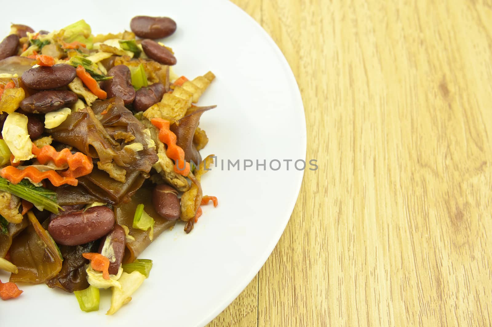 Fired thin noodles with soy sauce vegetarian in plate placed on brown wood background