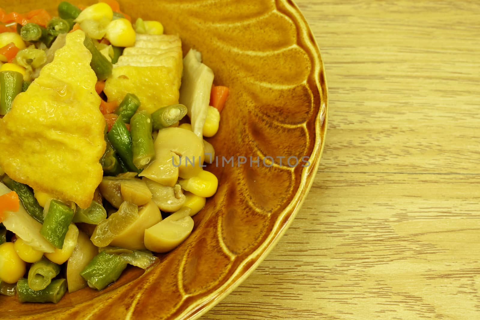 Tofu fried carrot, champignon mushroom, corn, vigna unguiculata sesquipedalis on dish with wood background.