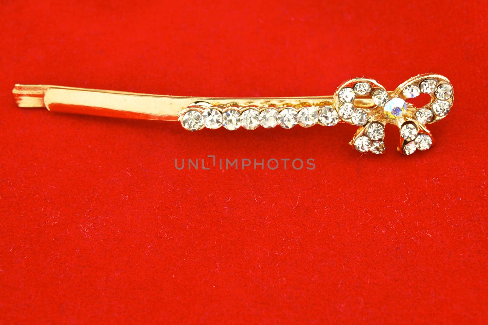 Gold hair clip and diamond as bow on red background.