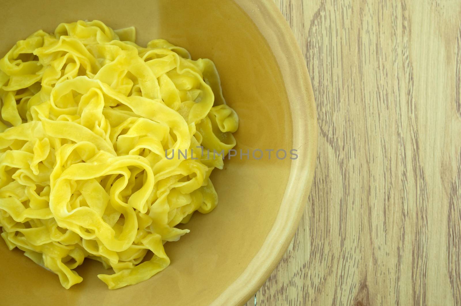 Close up big yellow noodle scald in brown bowl with wood background.