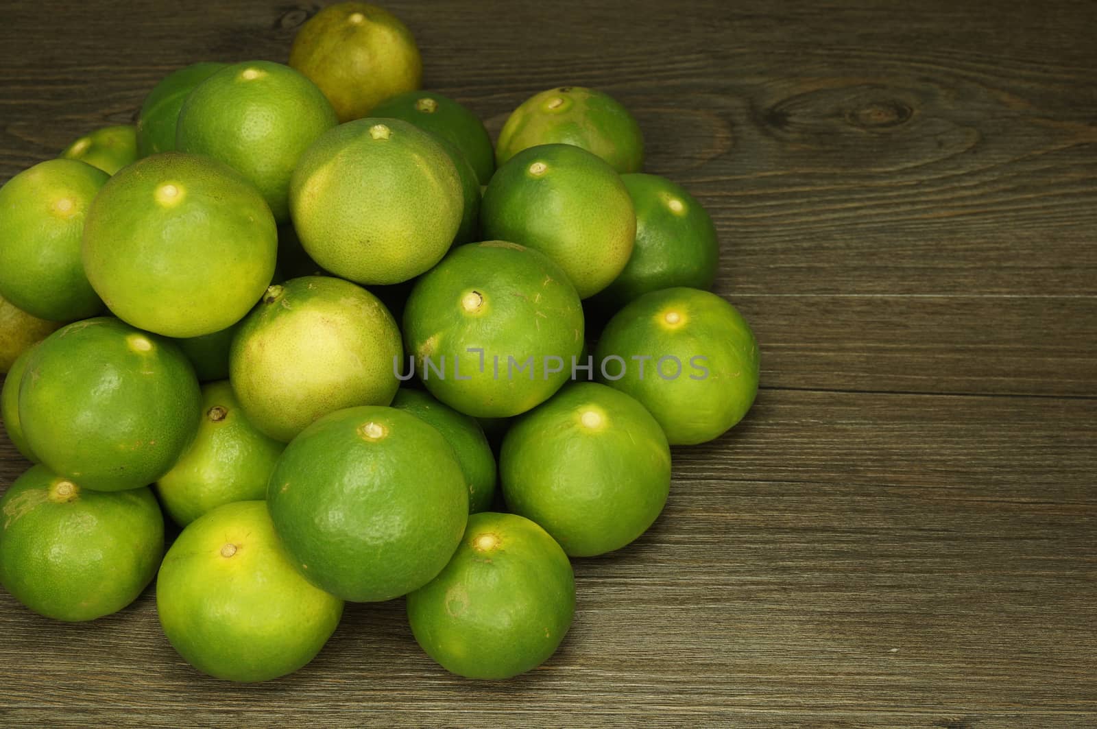 Pile of fresh green lemon place on left with wood background.