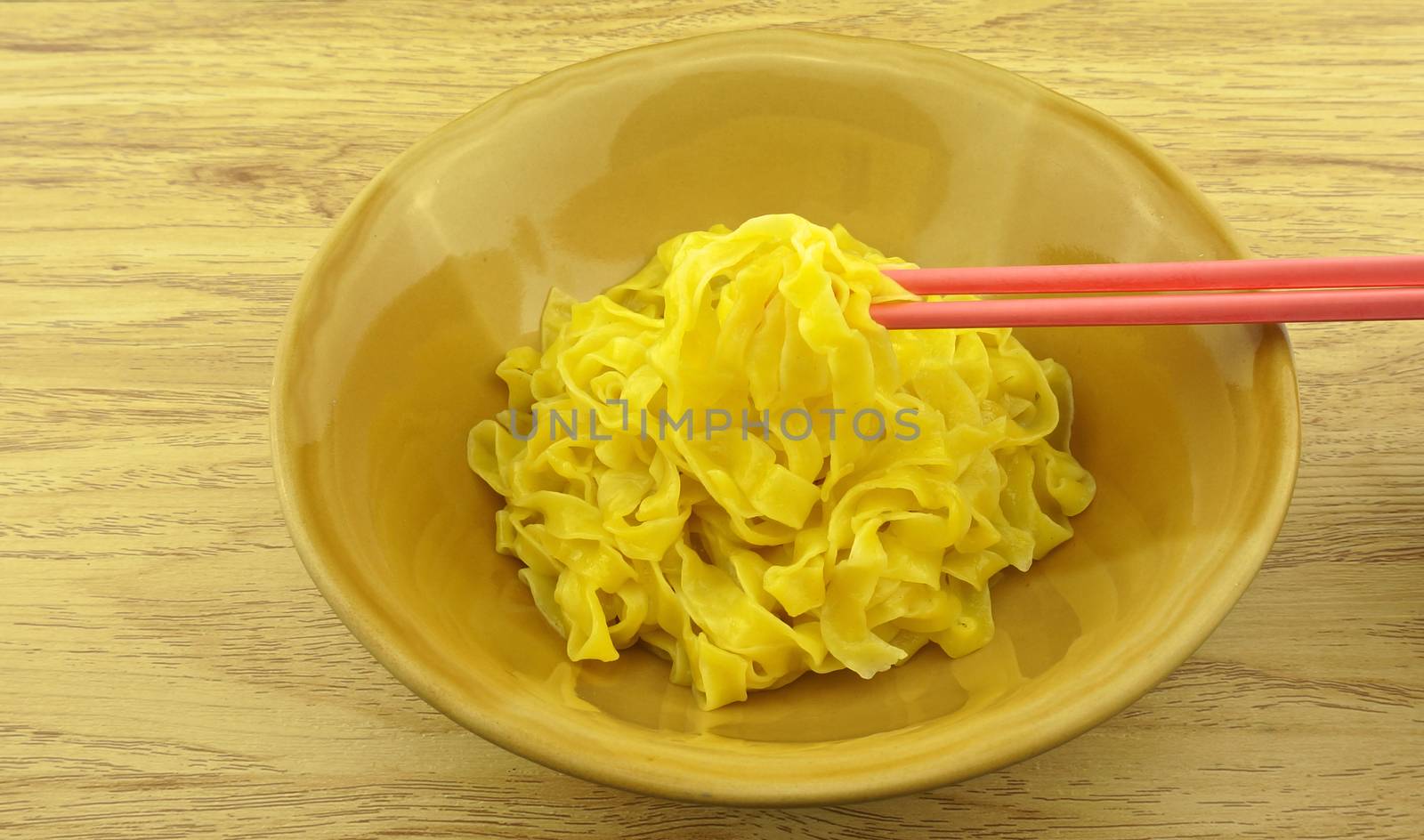 Eating big yellow noodle scald in brown bowl with chopsticks on wood background.