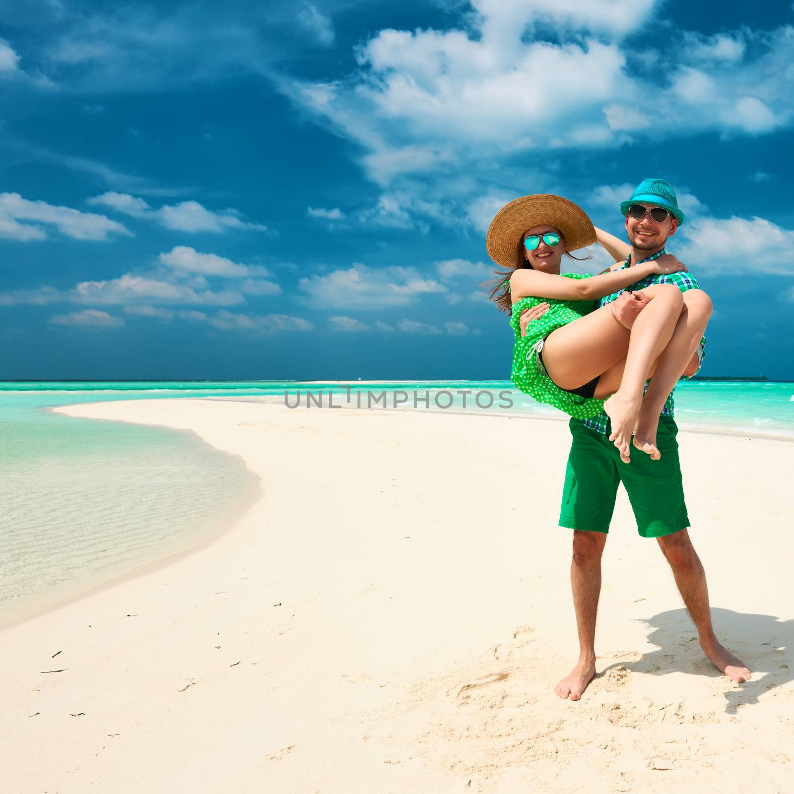 Couple in green on a tropical beach at Maldives. Man in holding woman on his arms.