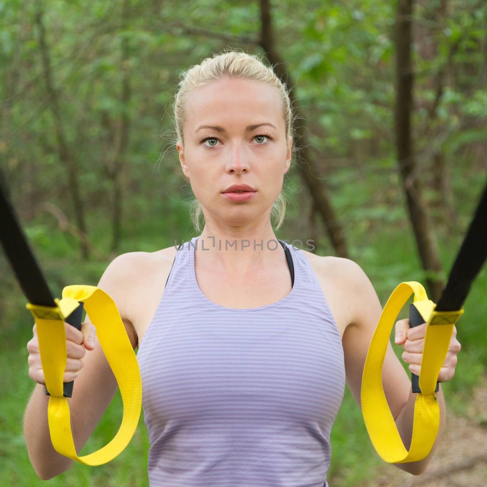 Young attractive woman does suspension training with fitness straps outdoors in the nature.