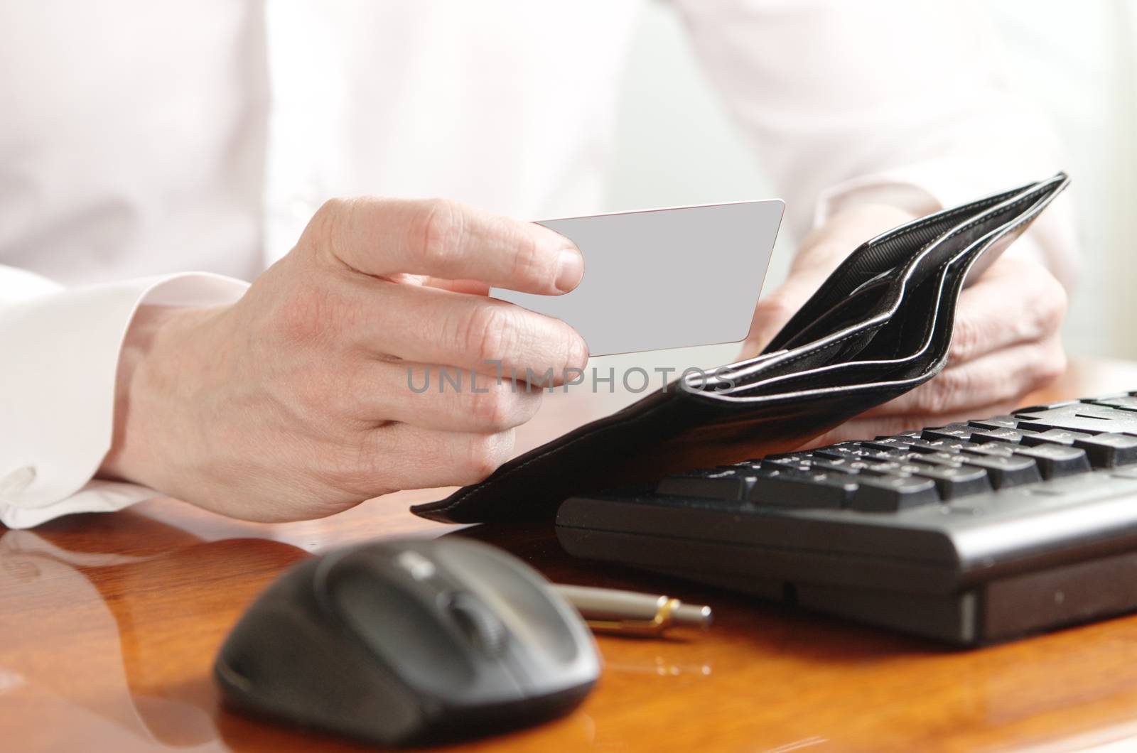 Hands of businessman with purse and bank card on the computer keyboard by Ravenestling