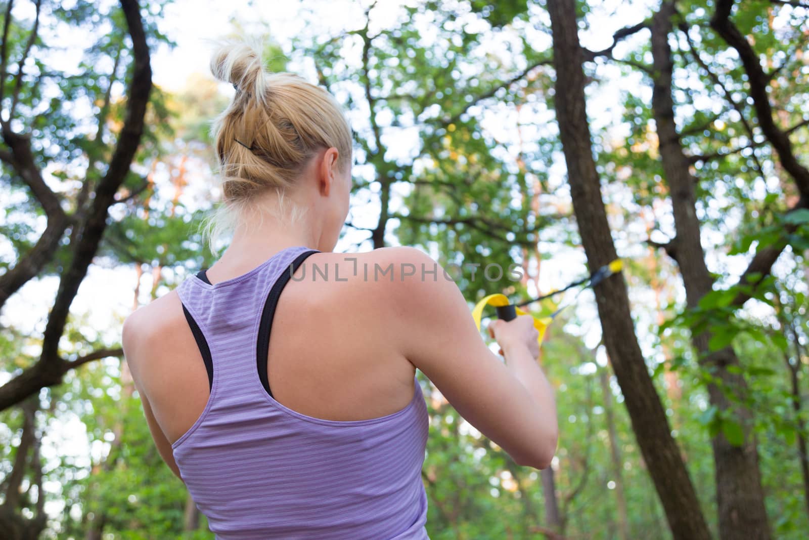 Young attractive woman does suspension training with fitness straps outdoors in the nature.