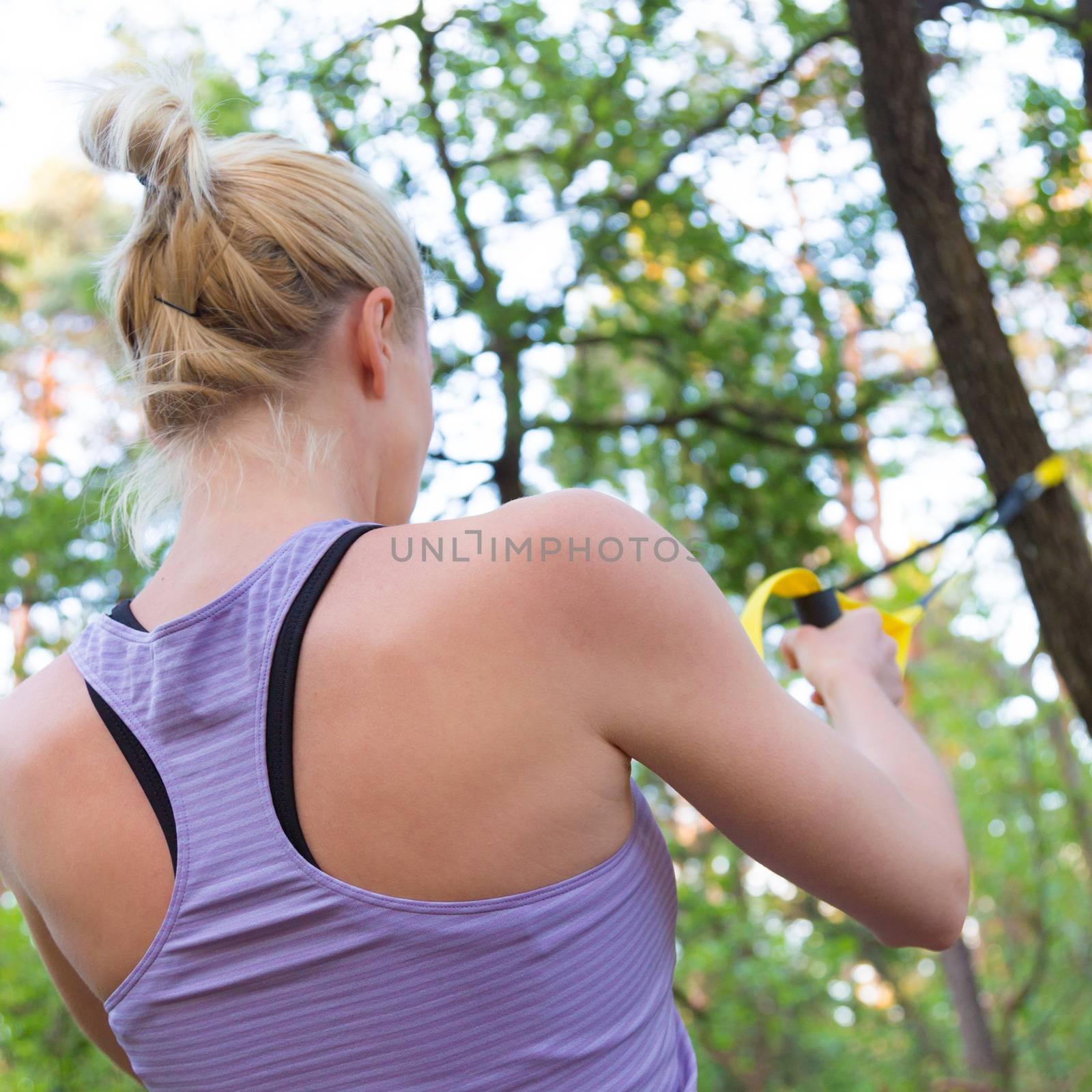 Young attractive woman does suspension training with fitness straps outdoors in the nature.