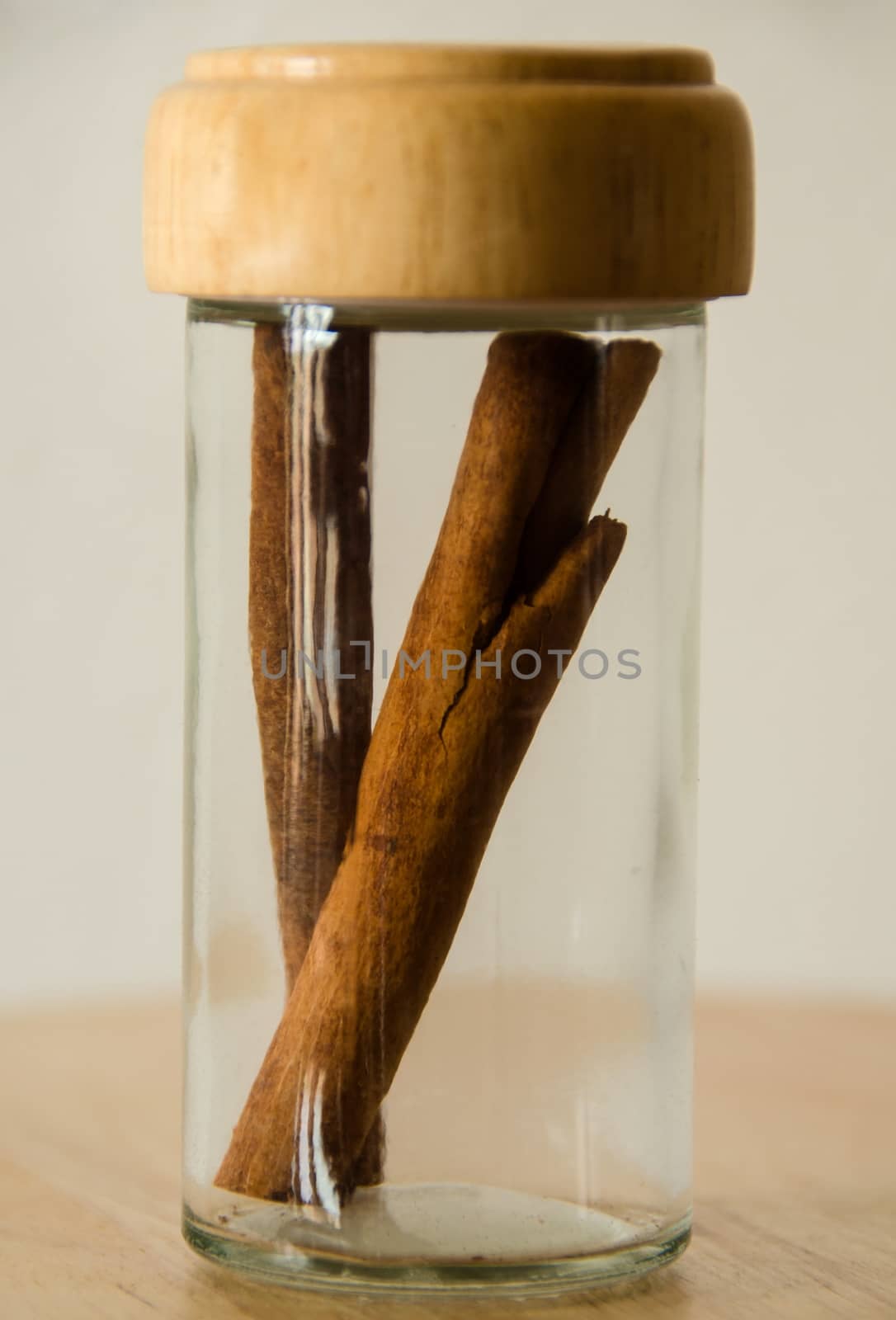 Cinnamon in the glass jar on wooden table, white background. 