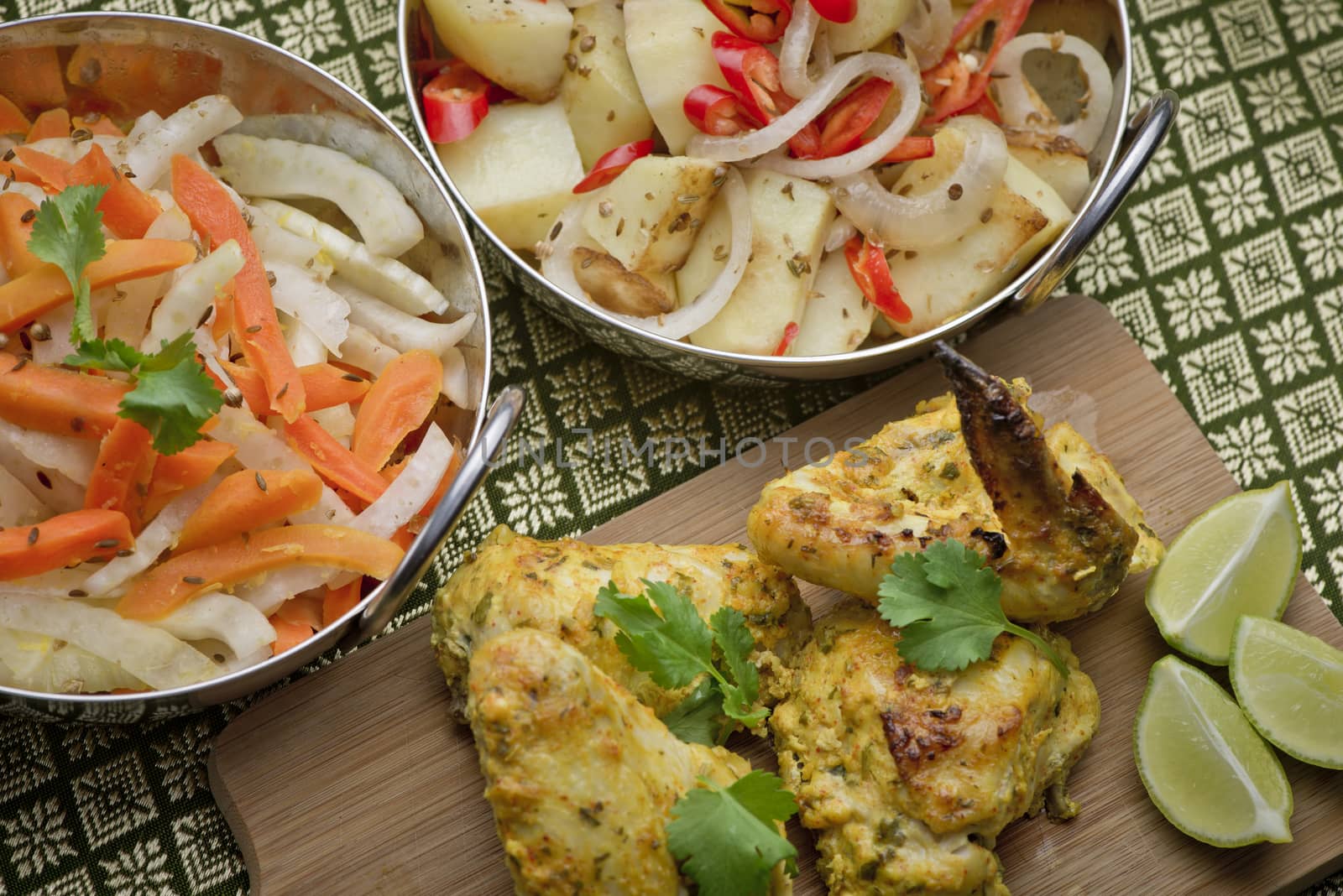 Indian chicken on a platter with bowls of salad and a garnish of lime, corriander and chili