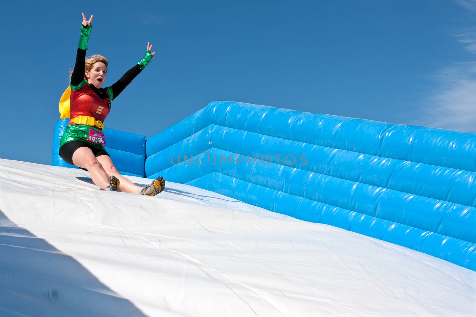 Atlanta, GA, USA - April 5, 2014:  A young woman wearing a Robin superhero costume enjoys sliding down a  plastic slide in the Ridiculous Obstacle Challenge (ROC) 5K race.