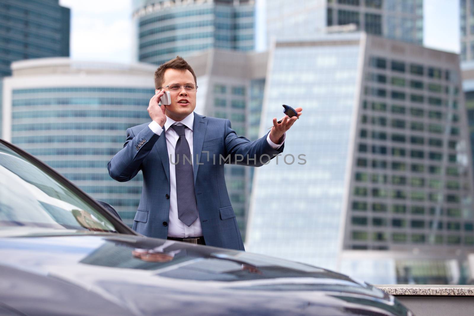 businessman on background of office near the car gives instructions over the phone and shows the hand