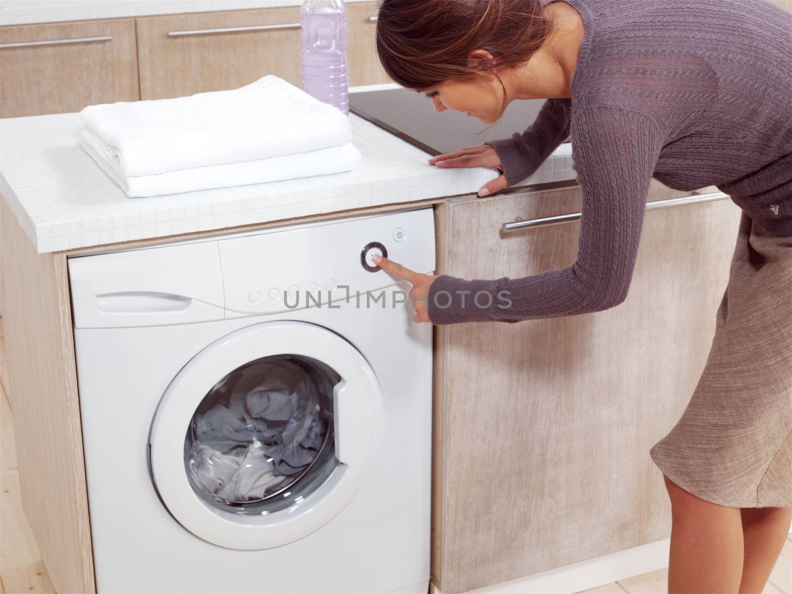 Close up of a young woman putting a cloth into washing machine 