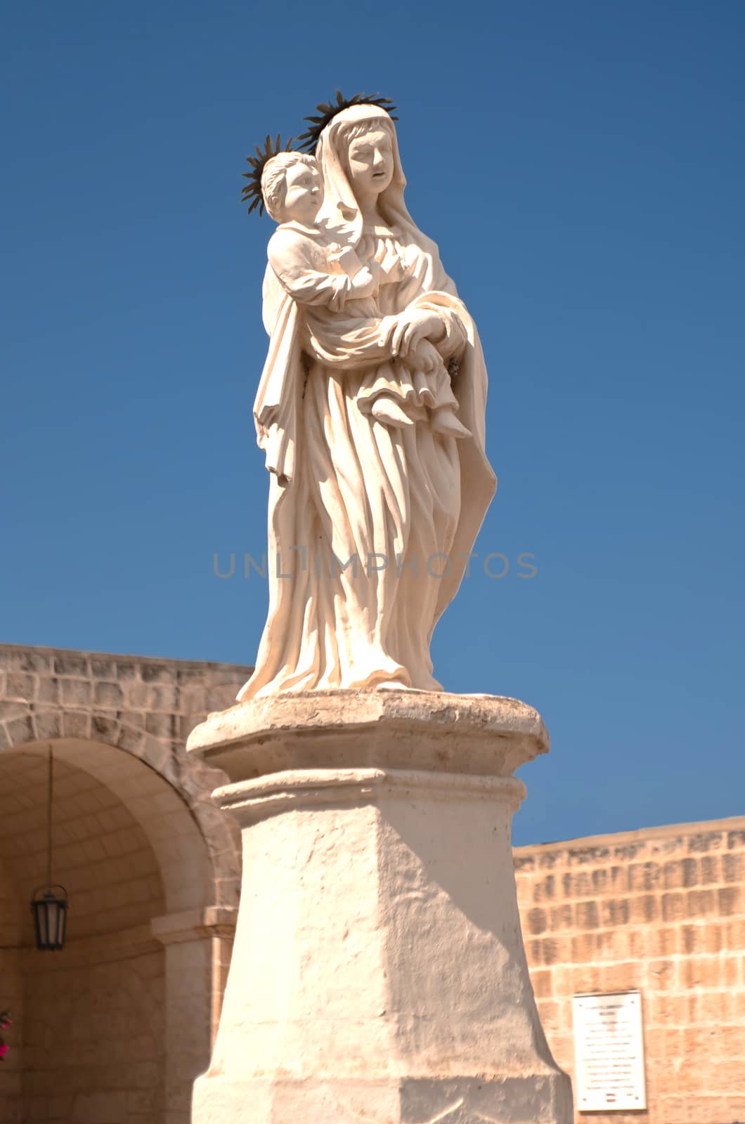 Statue of the Virgin Mary with the Baby in a little pedestrian plaza in front of the Church of the Our Lady of Mellieha - Mellieha, Malta.