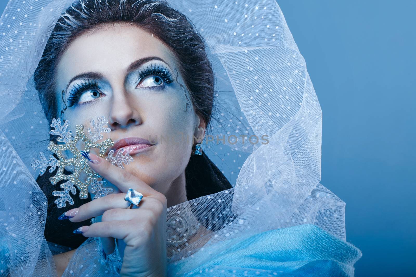 Girl with scenic make-up of the Snow Queen is holding a snowflake shot closeup