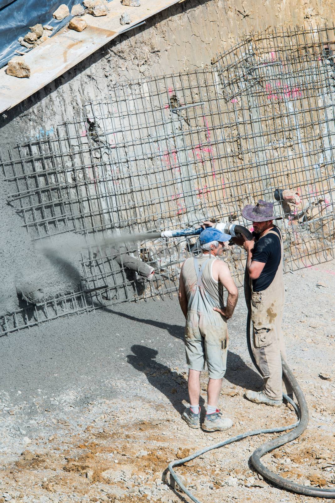 OSTFILDERN-SCHARNHAUSEN, GERMANY - MAY 22, 2014: A worker is aiming a pump tube while pouring concrete against the earth walls of a construction site whilst his colleague is chatting with him on May, 22, 2014 in Ostfildern-Scharnhausen near Stuttgart, Germany.