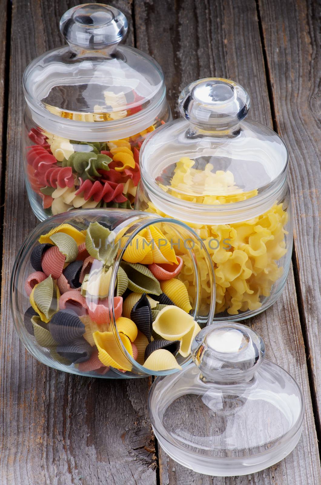 Arrangement of Colorful Conchiglie Pasta, Ballerine Pasta and Rotini Pasta in Glass Jars isolated on Wooden background