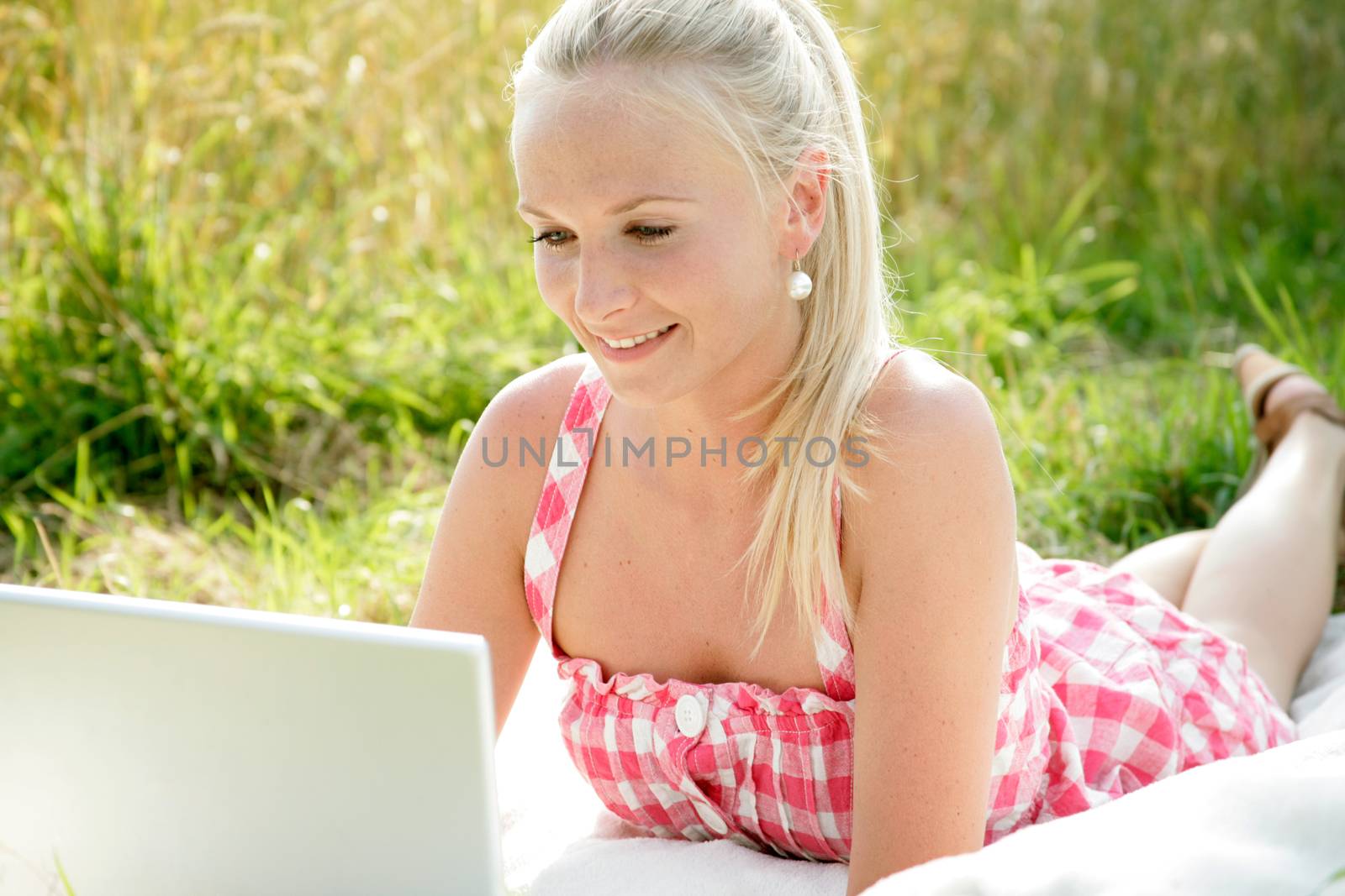 young attractive woman is lying on a blanket with computer in the open countryside