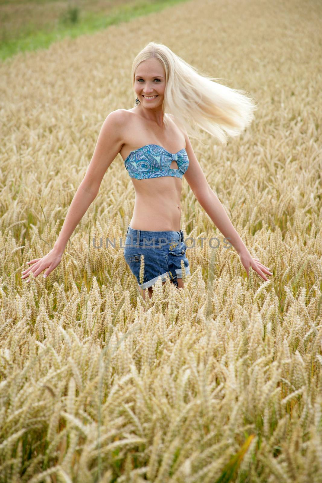 Young woman with bikini top and hot pants running through a wheat field She looks relaxed and cheerful.