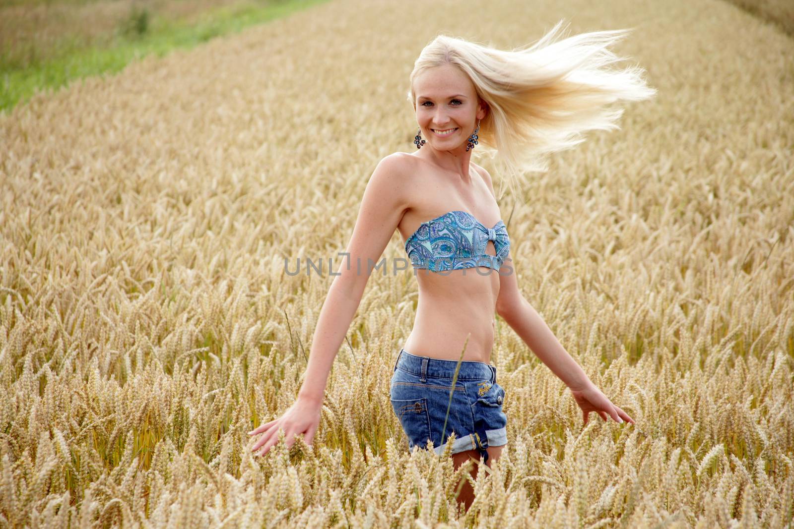 Young woman with bikini top and hot pants standing in a wheat field She looks relaxed and cheerful.