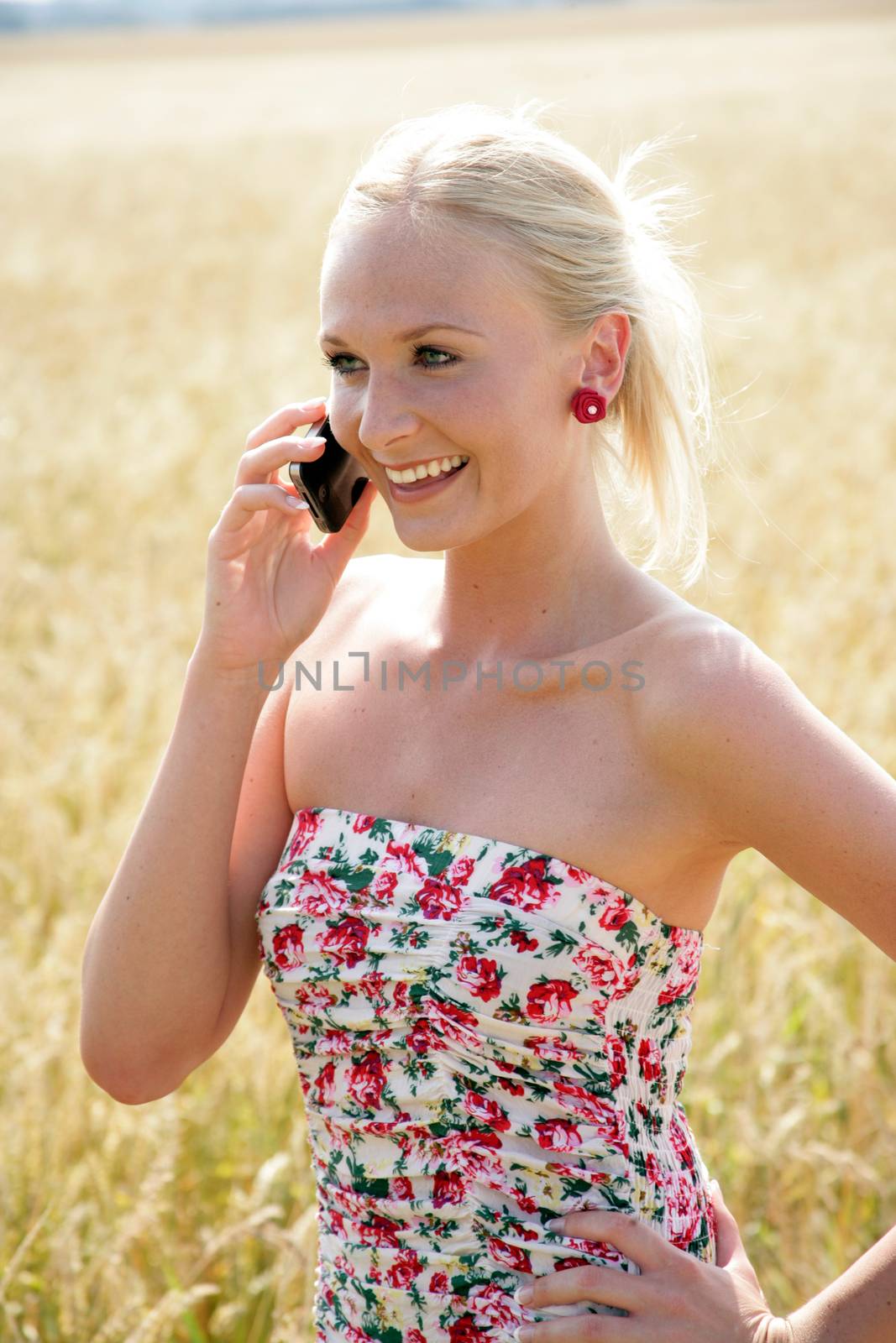 Young attractive woman is standing in a wheat field and speaks into her mobile phone. She looks happy and relaxed.