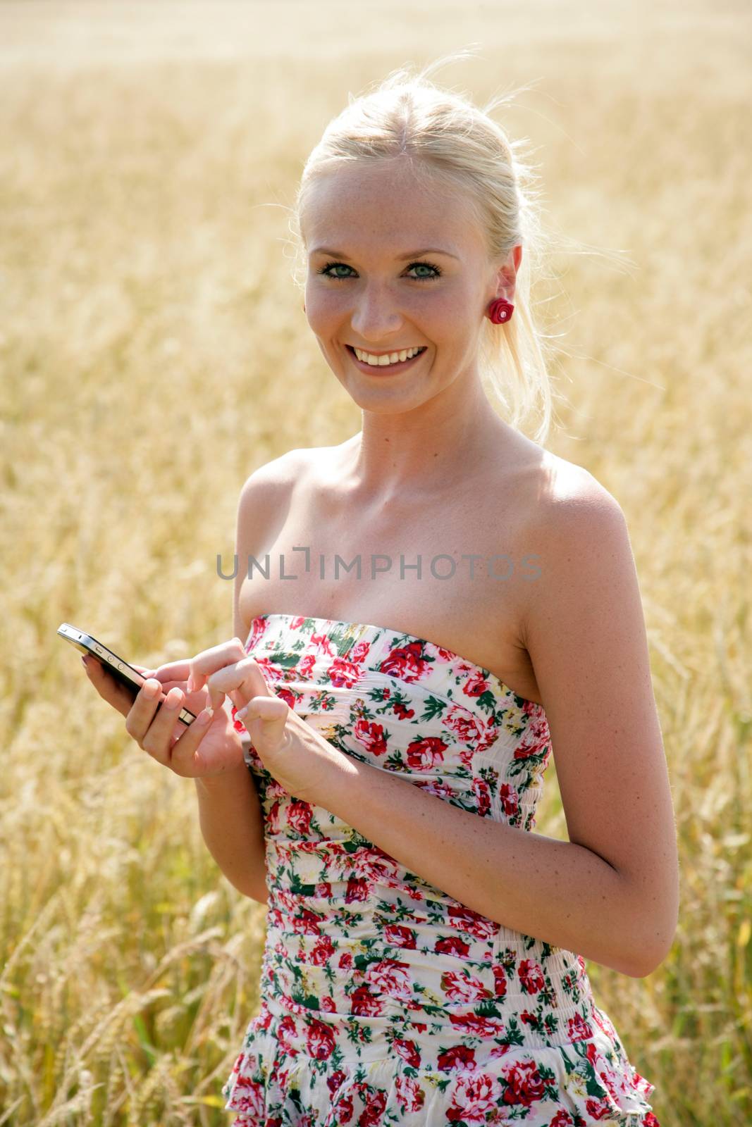 Young attractive woman standing in a wheat field, using her cellphone. She looks happy and relaxed.