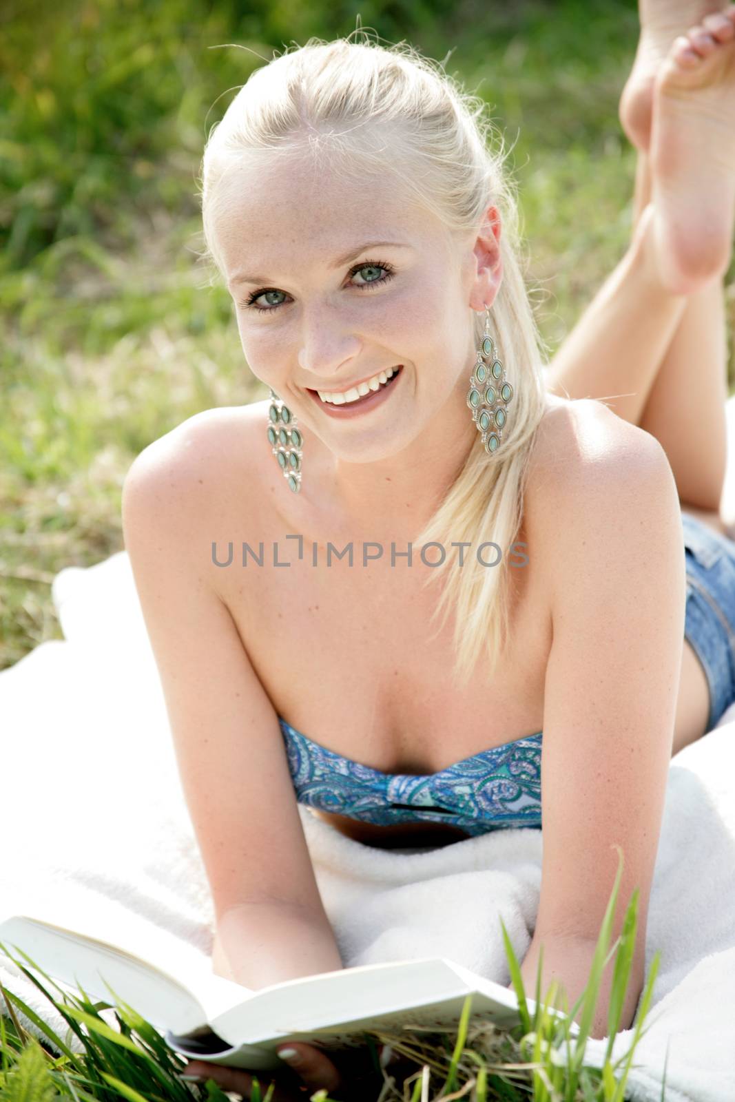 Young attractive woman lying on a blanket in the open countryside and reads a book. She looks relaxed and happy.