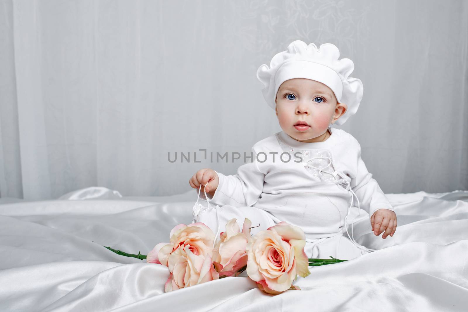 Little girl sitting on silk sheets lie at the feet of flowers