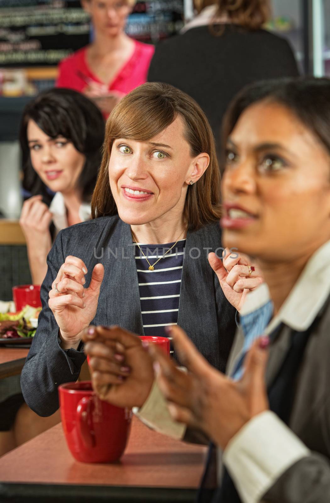 Business woman mocking coworker at table in cafeteria