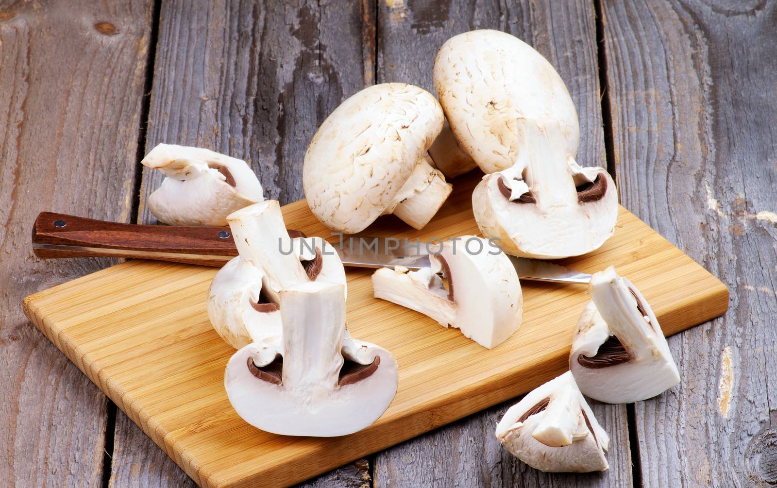 Raw Champignons Full Body and Slices with Kitchen Knife on Wooden Cutting Board closeup on Wooden background