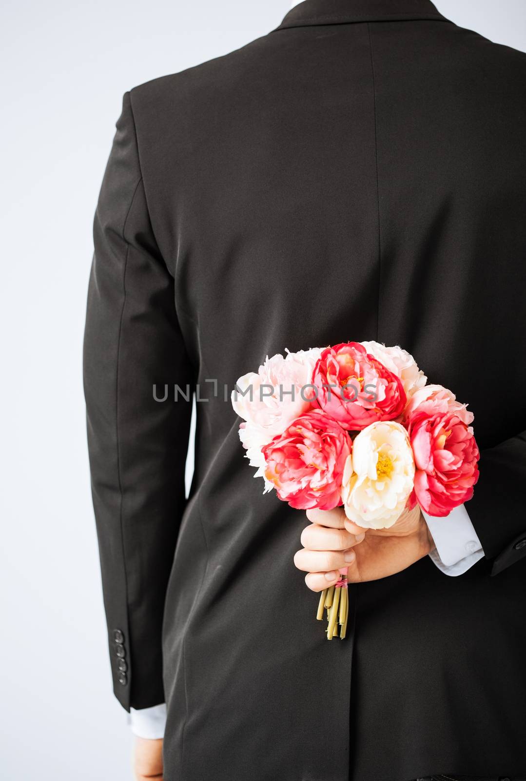 man hiding bouquet of flowers behind his back.