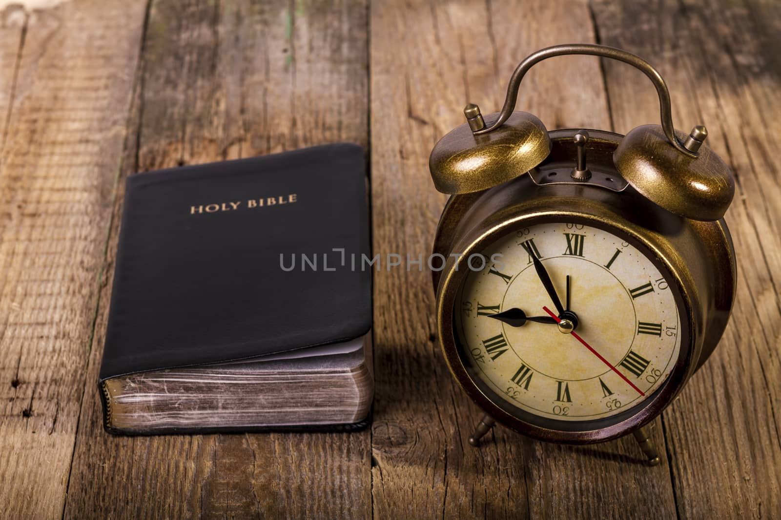 Holy Bible with clock on wood. Focus on clock.