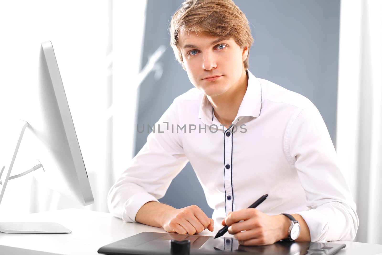 Portrait of handsome Caucasian man in a white shirt sitting in an office behind a desk