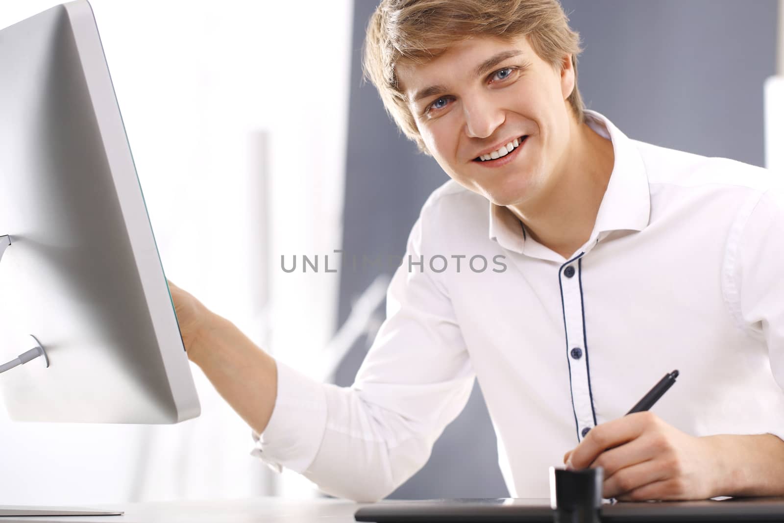 Portrait of handsome Caucasian man in a white shirt sitting in an office behind a desk