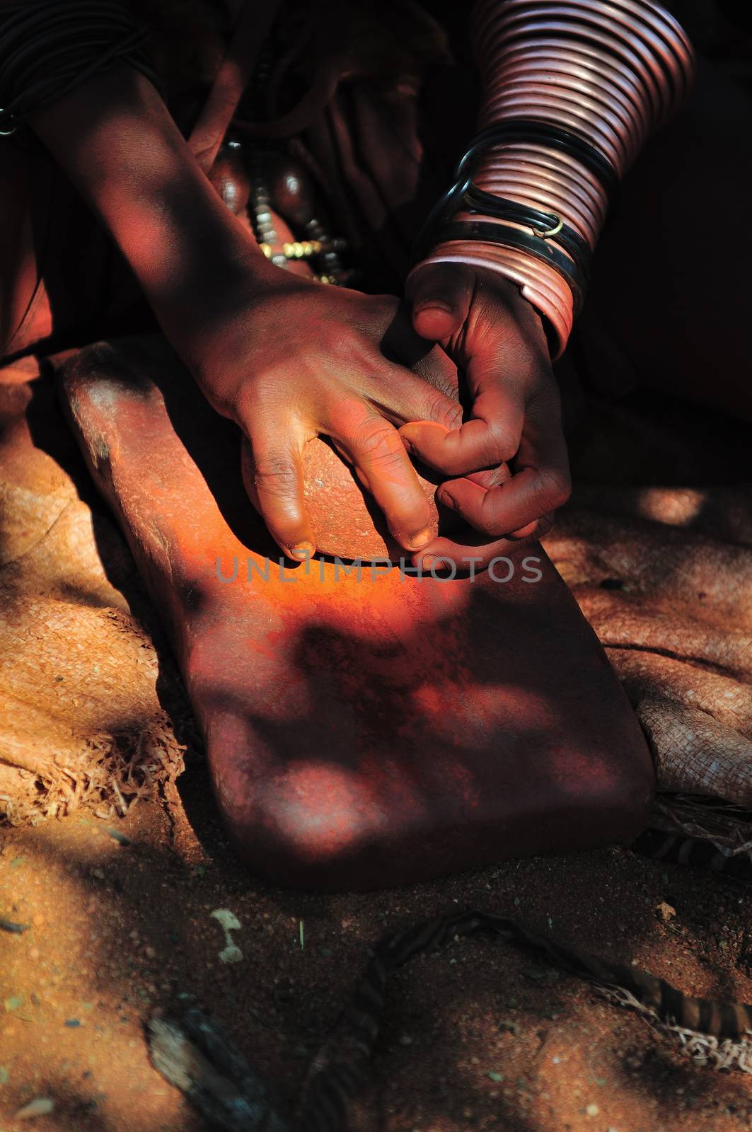 Himba woman grinding red ochre with a stone on another stone
