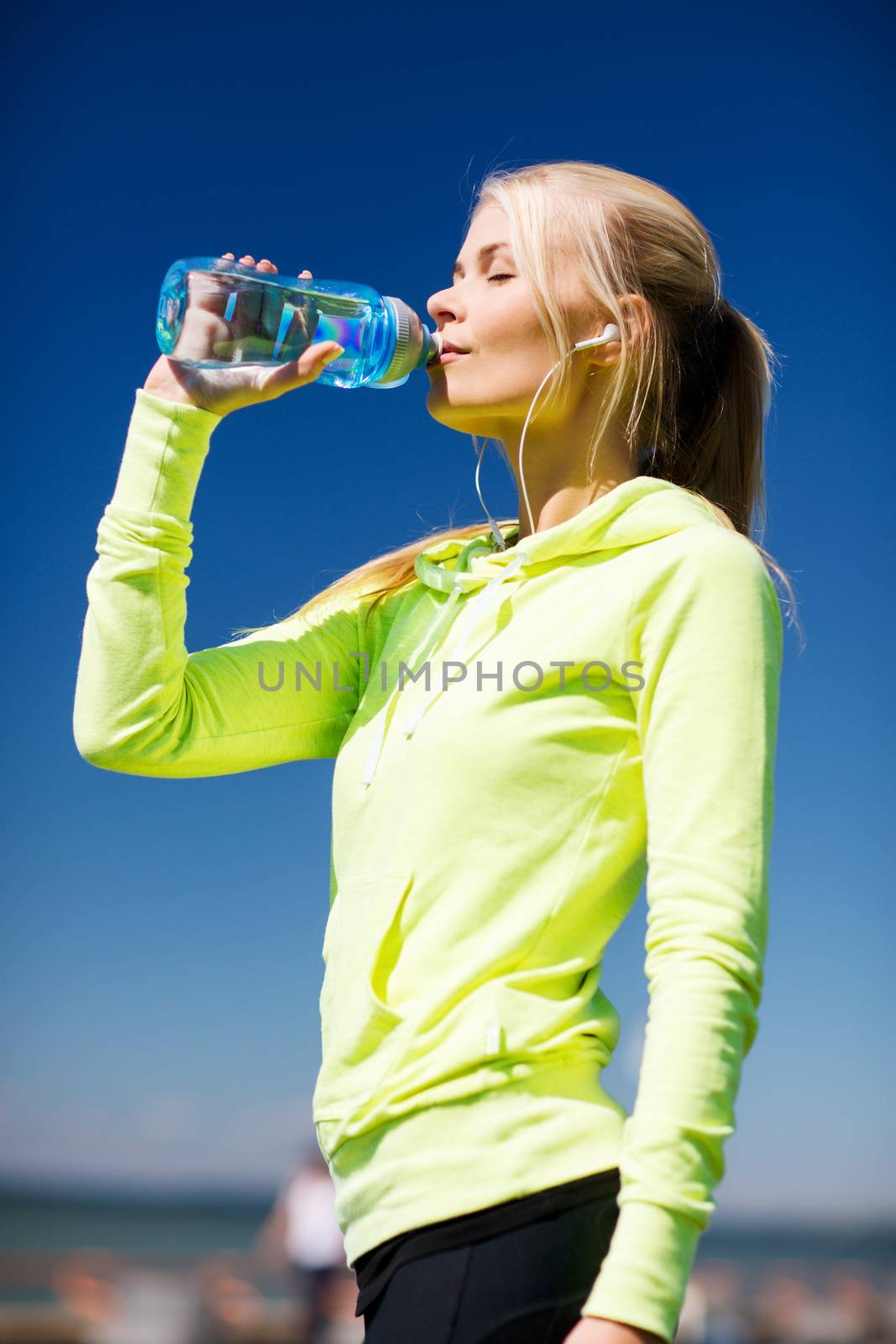 fitness and lifestyle concept - woman drinking water after doing sports outdoors