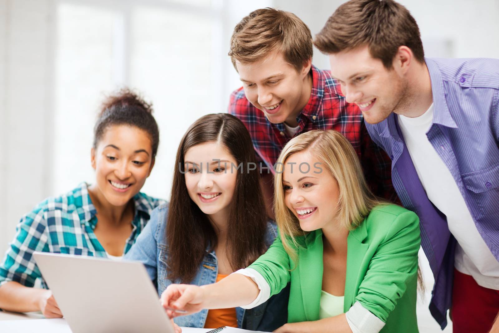 smiling students looking at laptop at school by dolgachov