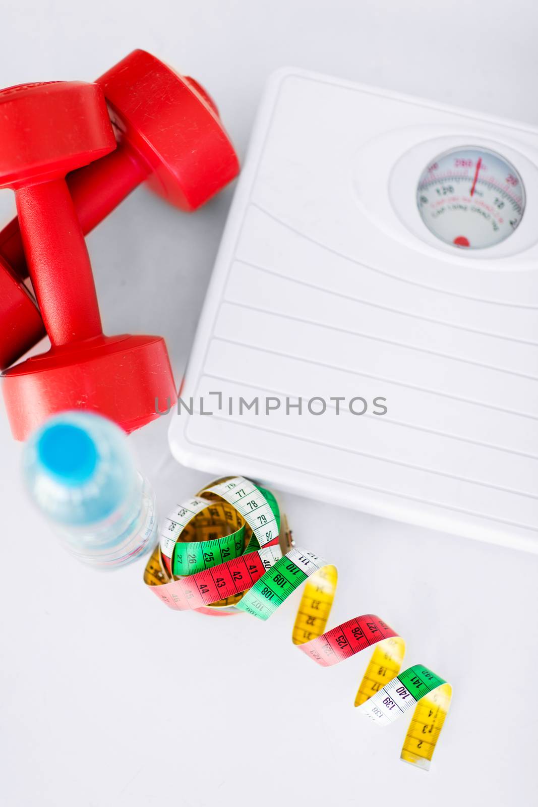 sport and diet concept - scales, dumbbells, bottle of water and measuring tape