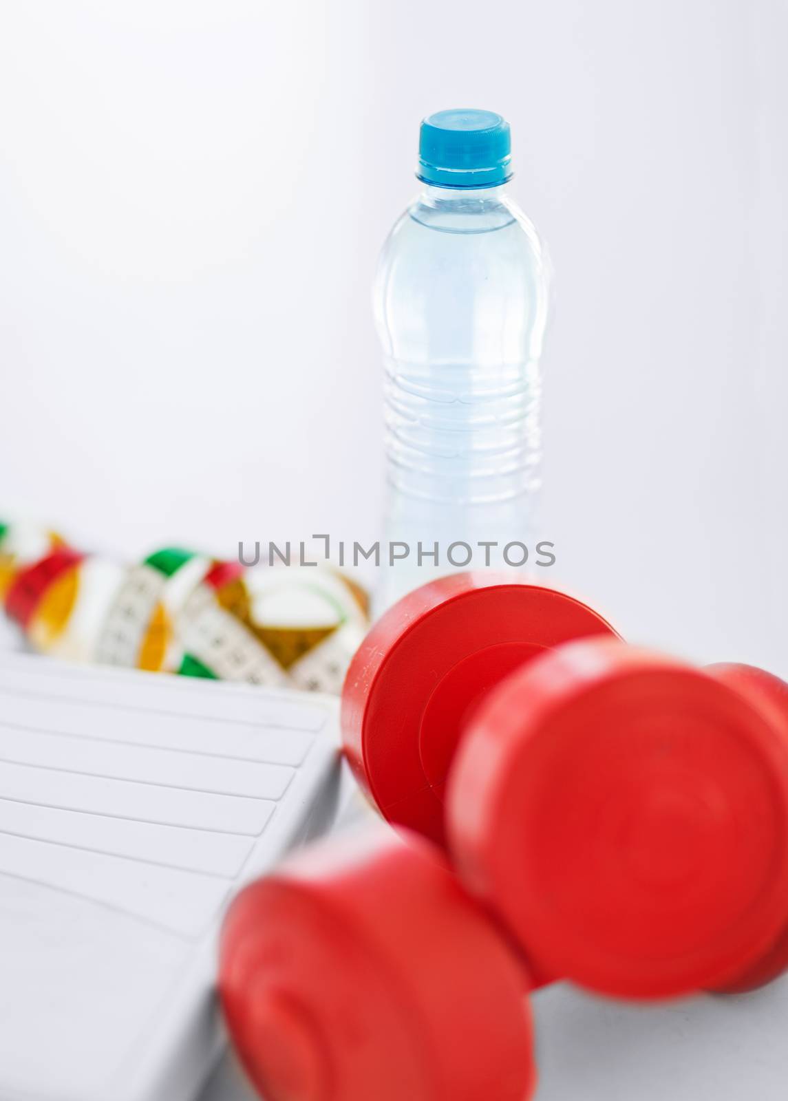 sport and diet concept - scales, dumbbells, bottle of water and measuring tape