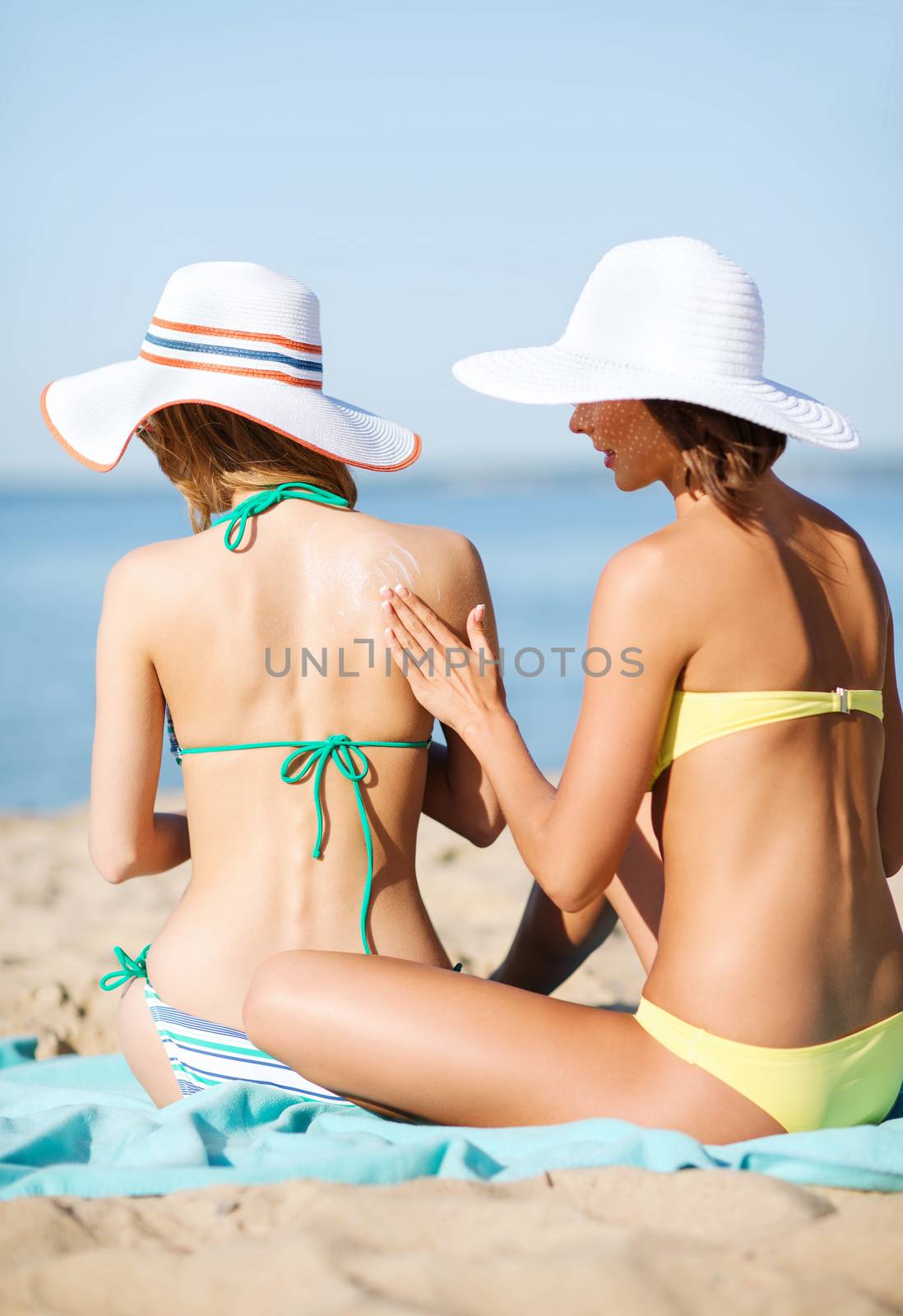 girls applying sun cream on the beach by dolgachov