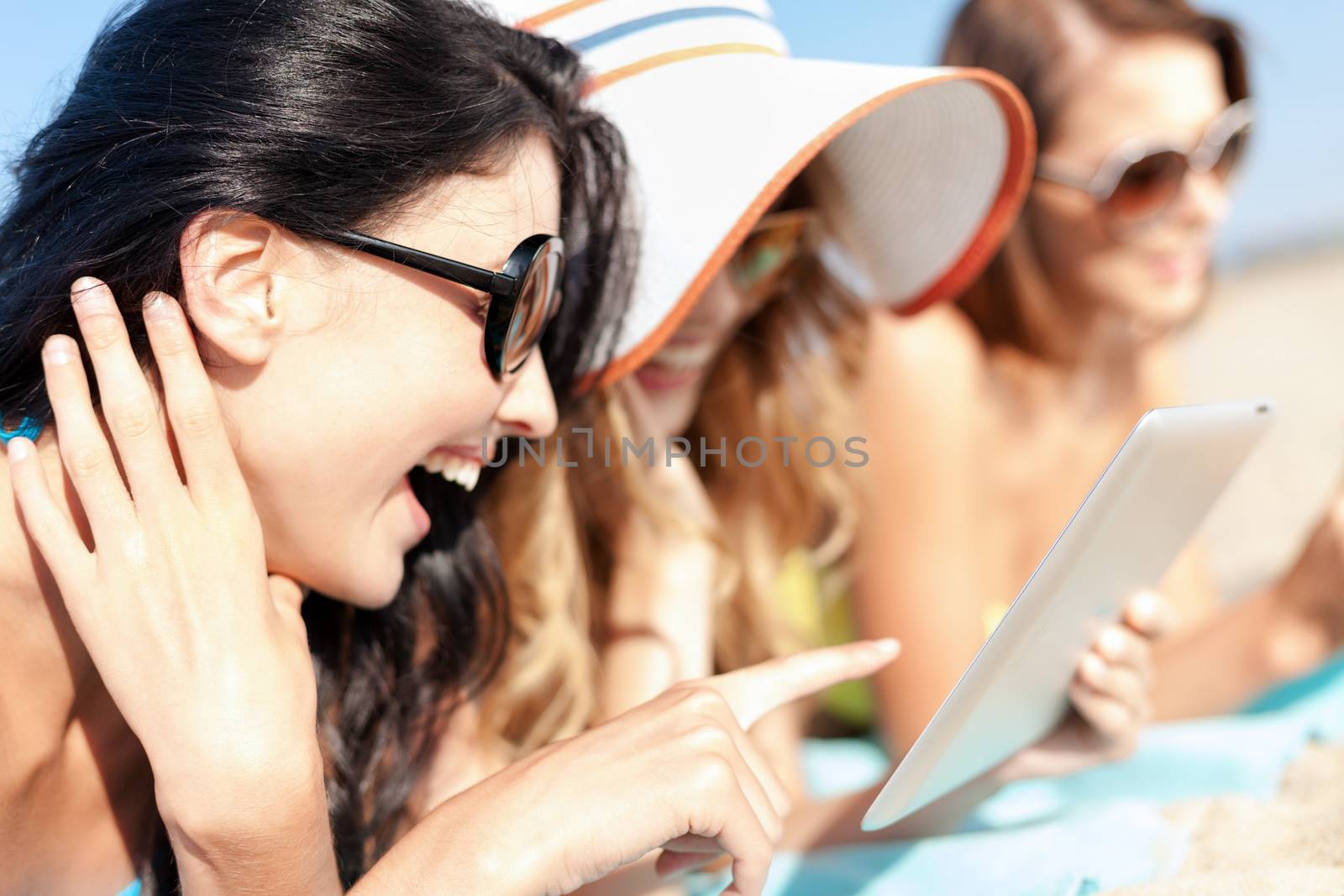 summer holidays, technology and internet concept - girls in bikinis with tablet pc sunbathing on the beach