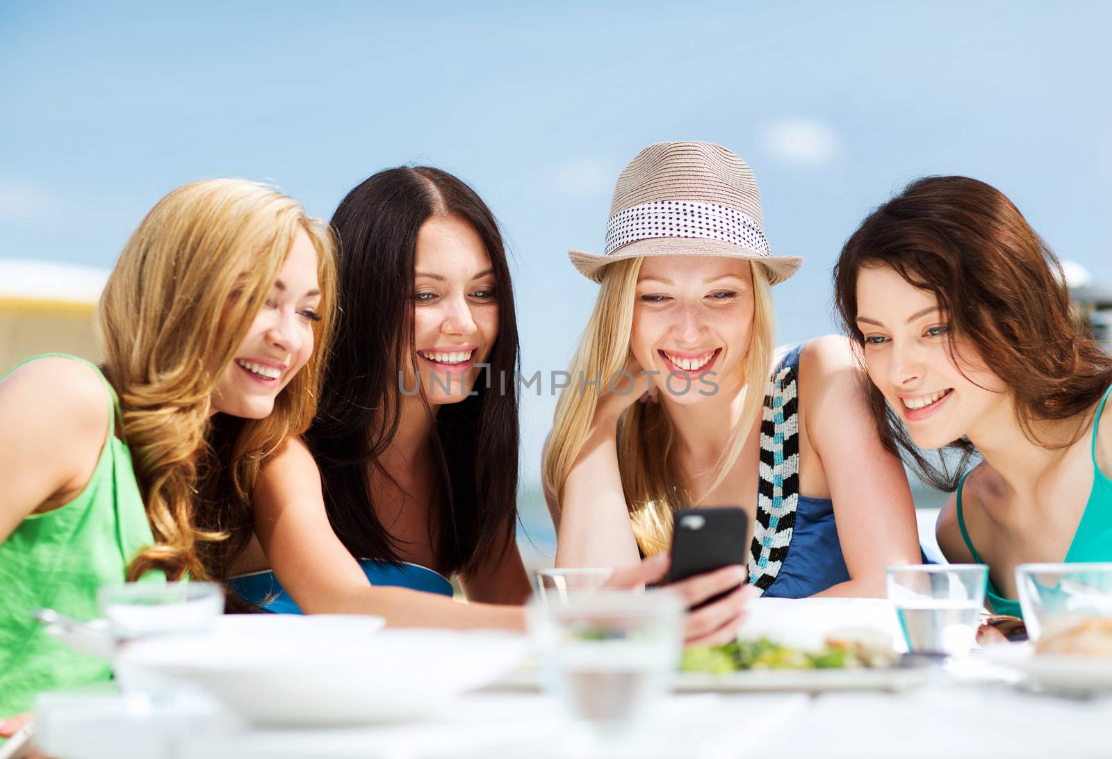 girls looking at smartphone in cafe on the beach by dolgachov